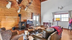 A cozy cabin interior with a fireplace, leather sofa, and wooden walls adorned with animal heads. - Spacious Mountain Chalet (Park County)