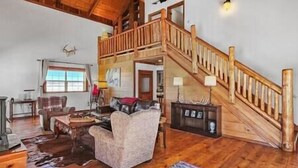 A spacious living room with a wooden staircase, a fireplace, and a large window. - Spacious Mountain Chalet (Park County)