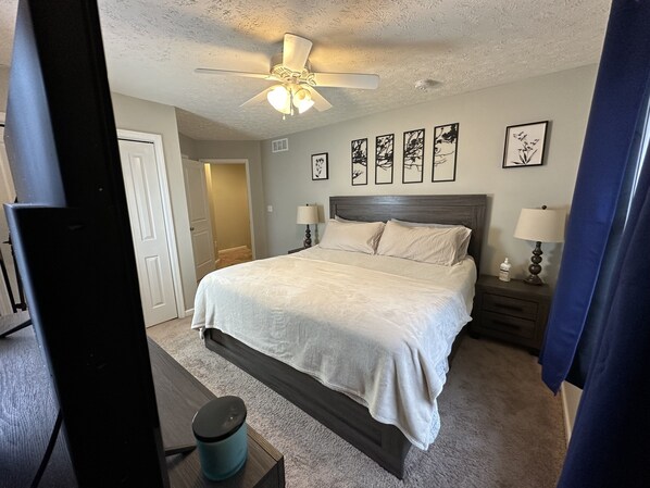 Een slaapkamer met een bed, een plafondventilator, een nachtkastje, een lamp en lijstwerken aan de wand.