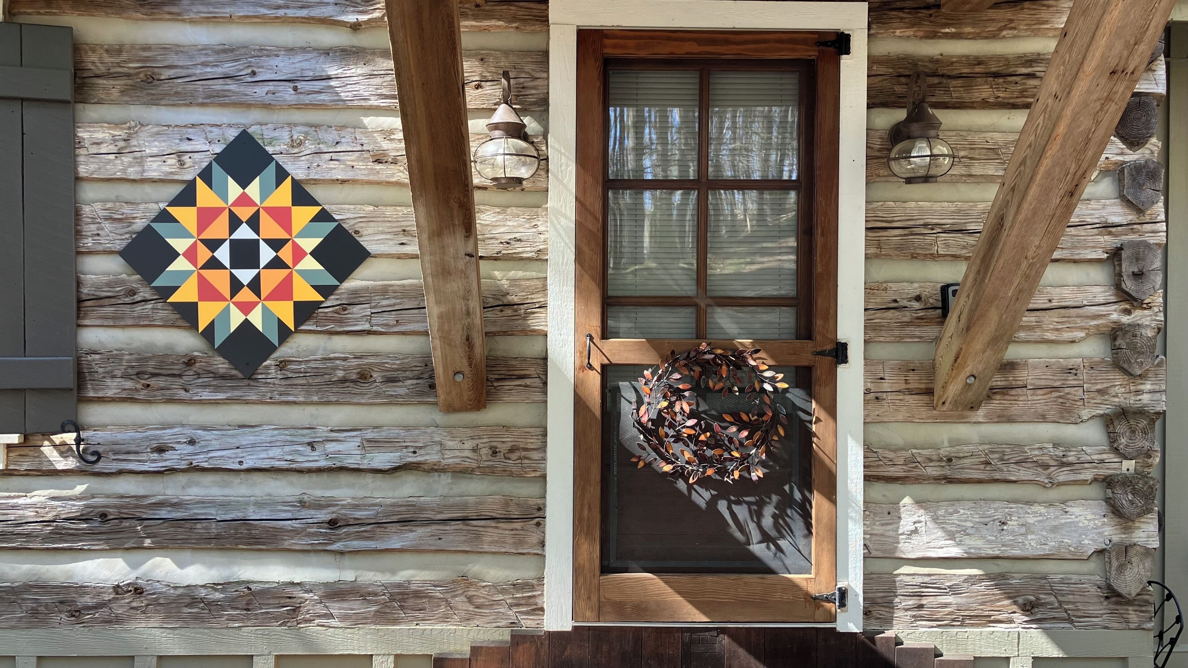 A rustic log cabin with a wooden door, a geometric wall decoration, and a wreath.