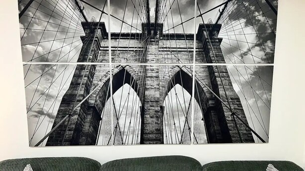 Fotografía en blanco y negro de un puente con un diseño de arco simétrico, expuesta en una pared sobre un sofá verde con cojines estampados.