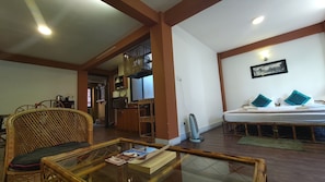 Una habitación con una cama, una silla de mimbre, una mesa de centro de vidrio y un rincón americano.