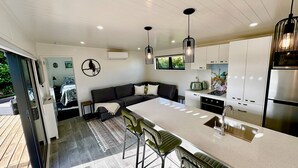 A modern kitchen with a central island, bar stools, and a built-in oven. - Modern 2 Bedroom, 2 Bathroom Cottage with Farm Views (Bombay)