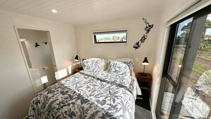 A bedroom with a bed, two bedside tables, a window, and a door. - Modern 2 Bedroom, 2 Bathroom Cottage with Farm Views (Bombay)