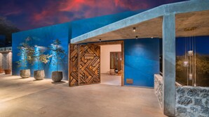 Un edificio moderno con fachada azul, un panel de madera geométrico y plantas en macetas.