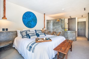 Un dormitorio moderno con una cama grande, un banco de madera, una lámpara colgante y una obra de arte azul de gran tamaño.
