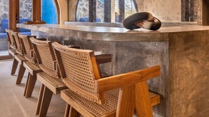 Un área de bar moderna con sillas de madera, una barra y lámparas colgantes.