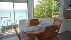 A dining area with a table and chairs, a view of the sea through large windows, and a kitchen area with a tiled backsplash. - Résidence de la vieille tour  (Le Gosier)