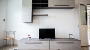 A modern living room with a flat-screen TV on a grey console, a chair, and a small table with a vase.