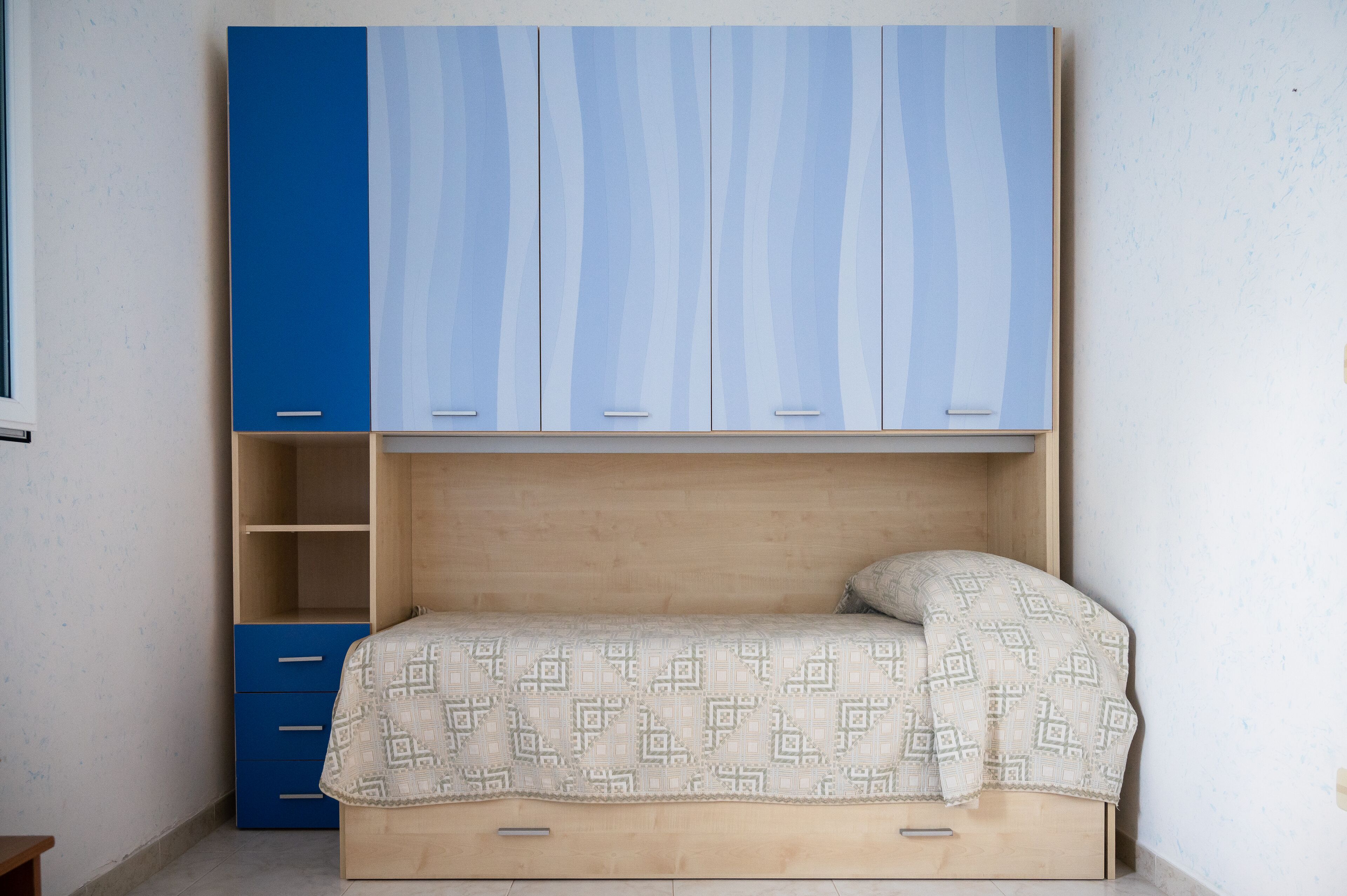 A bedroom with a bed, a blue wardrobe, and a wooden nightstand.