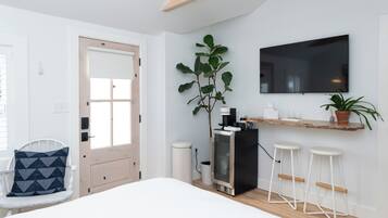 A modern room with a bed, a TV mounted on the wall, a coffee machine, and a plant.