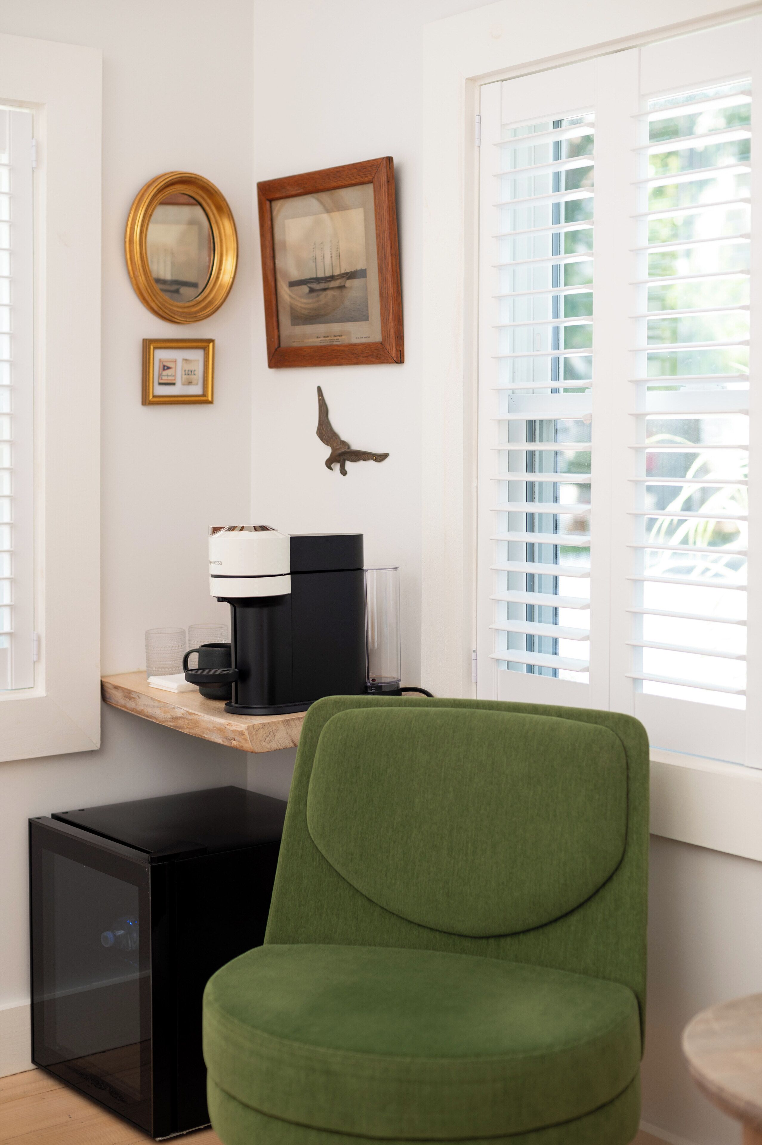 A room with a green chair, a coffee machine, a framed picture, and a small table.