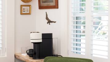 A room with a green chair, a coffee machine, a framed picture, and a small table.