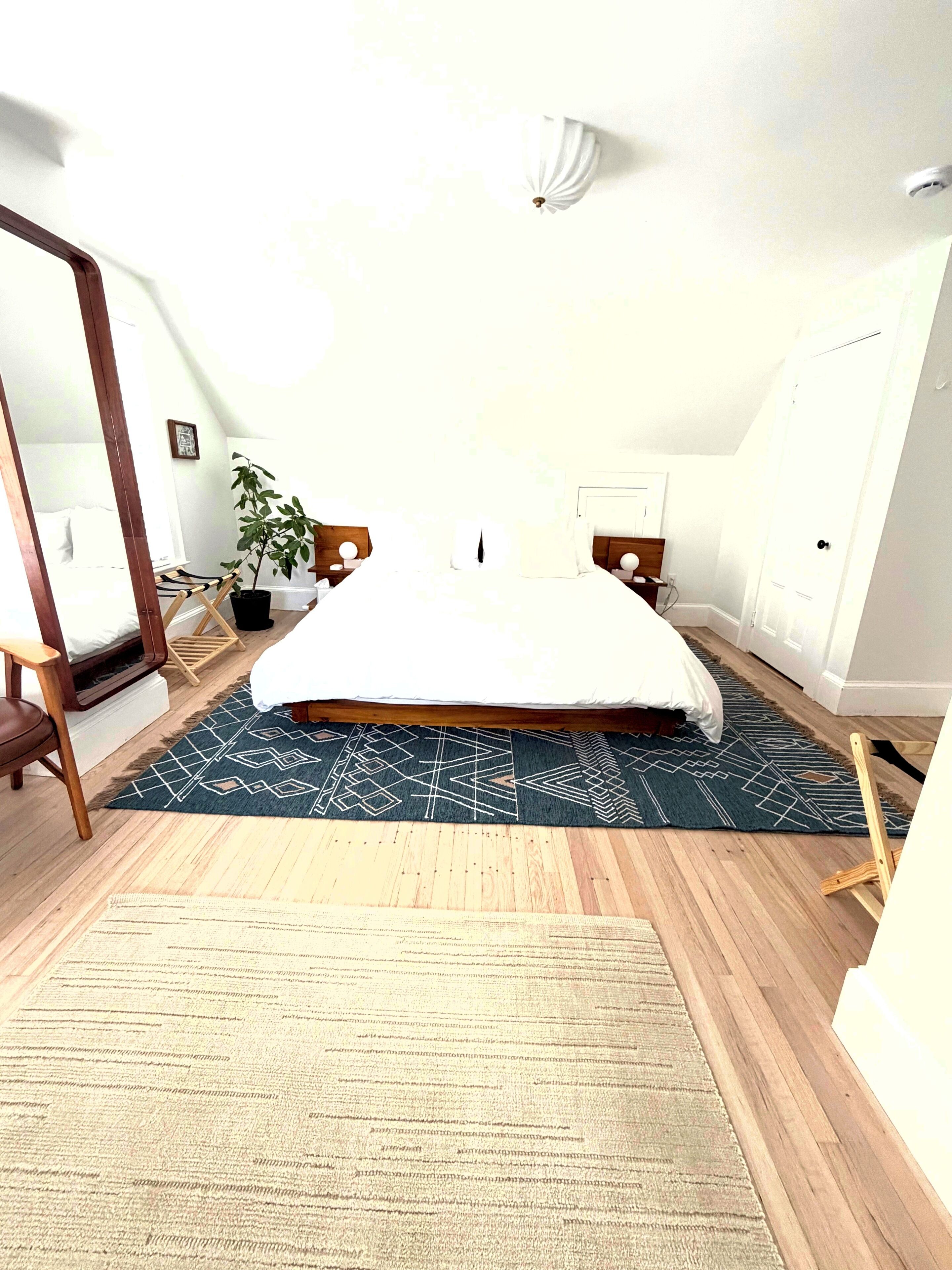Un dormitorio con cama, planta en maceta, suelo de madera y espejo.