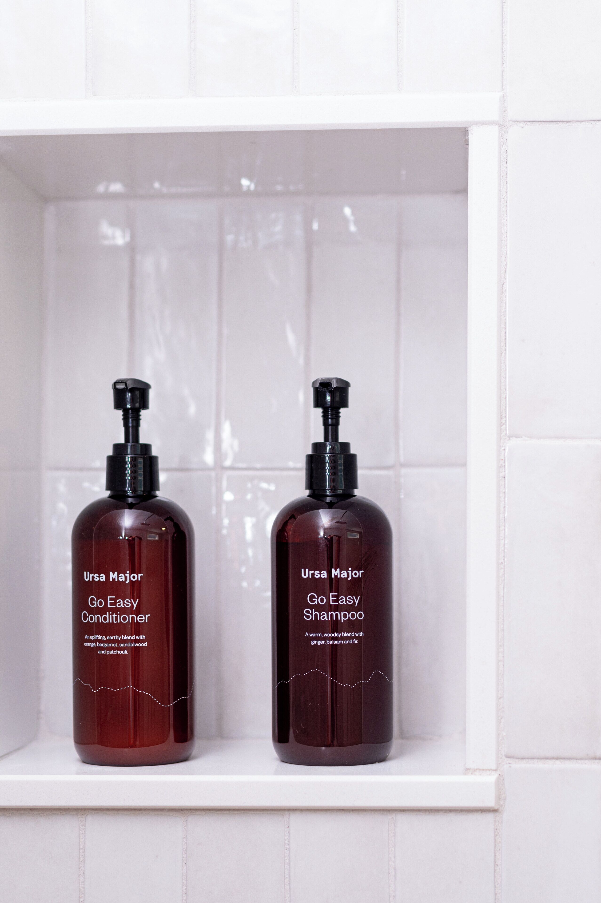 Two bottles of Ursa Major Go Easy Conditioner and Shampoo on a white shelf.