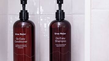 Two bottles of Ursa Major Go Easy Conditioner and Shampoo on a white shelf.