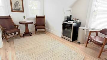 A room with a large rug, two wooden chairs, a small table, a fireplace, and a framed picture on the wall.