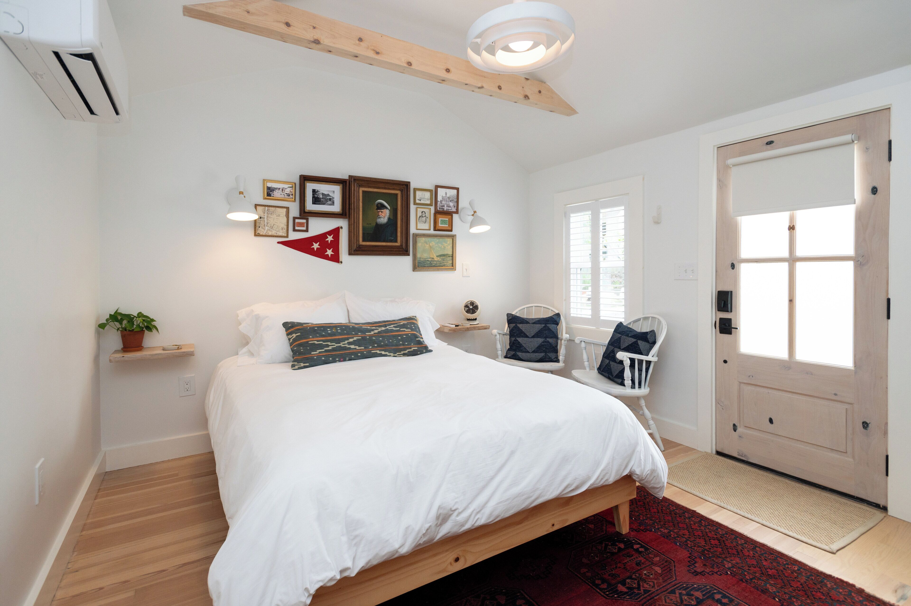 A bedroom with a bed, a chair, a door, and a wall with framed pictures.