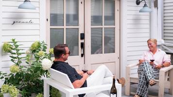 A porch with two white chairs, a potted plant, and a bottle of wine.