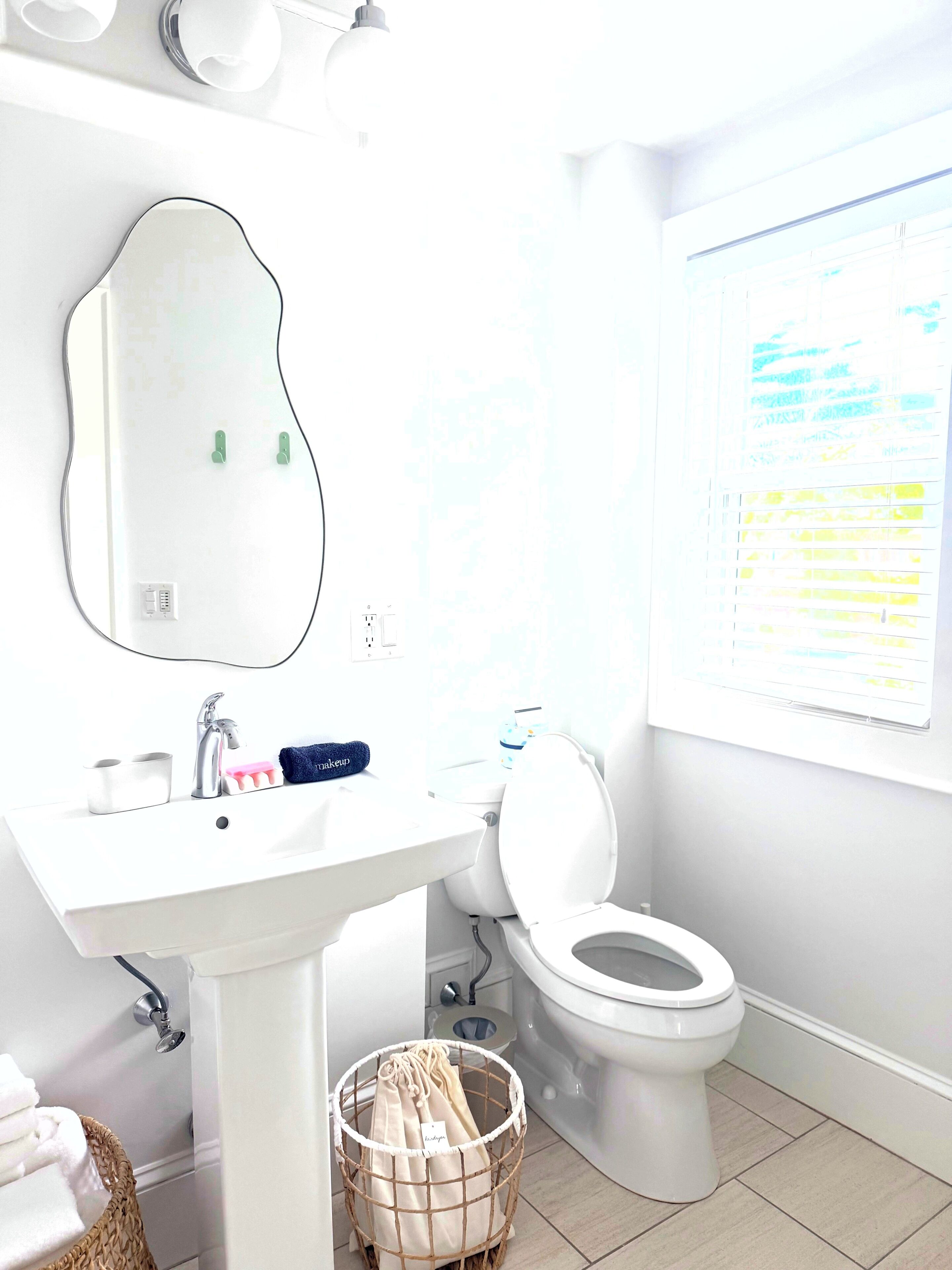Un baño con un lavamanos blanco, espejo, inodoro y ventana.