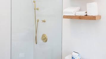 Ein modernes Badezimmer mit Duschkabine aus Glas, einem hölzernen Ablagebrett mit Handtüchern und einem WC mit einer Wasserflasche darauf.