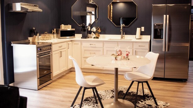 A modern kitchen with dark walls, white cabinetry, a central island, and a dining area with two chairs. - Suite 101 is the Main House's largest and most luxurious suite. (Cherokee Village)