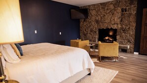 A bedroom with a bed, a stone wall, a fireplace, and a small table. - Suite 101 is the Main House's largest and most luxurious suite. (Cherokee Village)