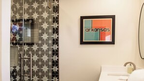 A bathroom with a glass shower enclosure, a sink with a mirror, and a framed picture on the wall. - Suite 103 also known as the Arkansas Suite (Cherokee Village)