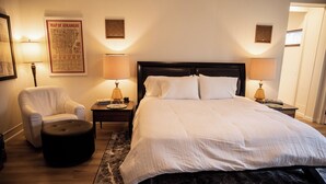 A neatly arranged bedroom with a large bed, two bedside tables with lamps, a chair, and a rug. - Suite 103 also known as the Arkansas Suite (Cherokee Village)
