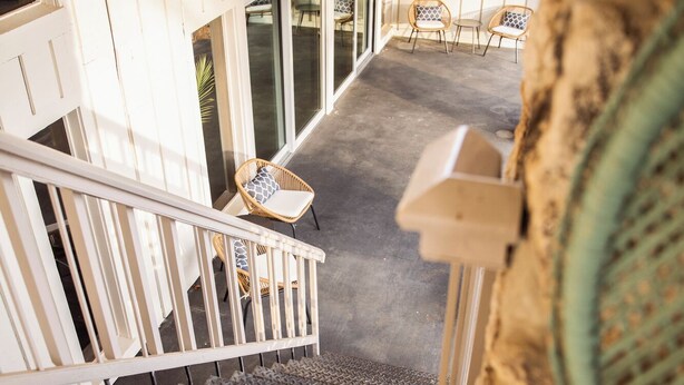 A wooden deck with a metal railing, a wicker chair, and a view of the outdoor area. - Suite 104 freatures a private outdoor-covered balcony. (Cherokee Village)