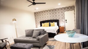 A modern bedroom with a bed, grey sofa, ottoman, and a small round table with a blue bowl. - Suite 104 freatures a private outdoor-covered balcony. (Cherokee Village)