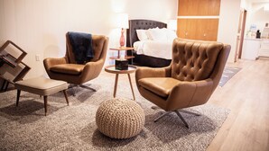 A hotel room with a bed, two armchairs, a small table, a round ottoman, and a bookshelf. - Suite 105 freatures a private outdoor-covered balcony. (Cherokee Village)
