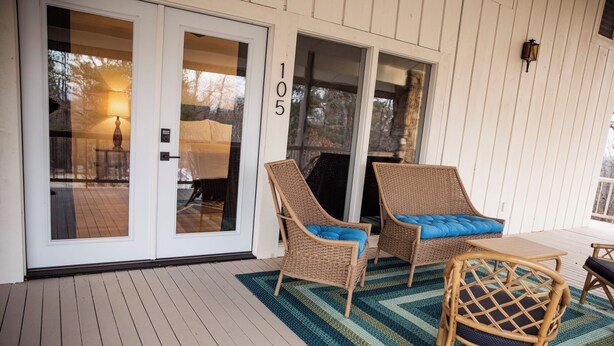 A covered porch with wicker chairs and a table, a sliding glass door, and a number '105' on the wall. - Suite 105 freatures a private outdoor-covered balcony. (Cherokee Village)