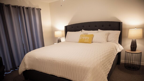 A neatly made bed with a headboard, two bedside lamps, and a pillow with text.
