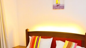 Una cama bien tendida con sábanas blancas, una colcha marrón y almohadas a rayas de colores.