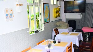 Un comedor con mesas dispuestas para dos, un televisor en la pared y un mapa colgado.
