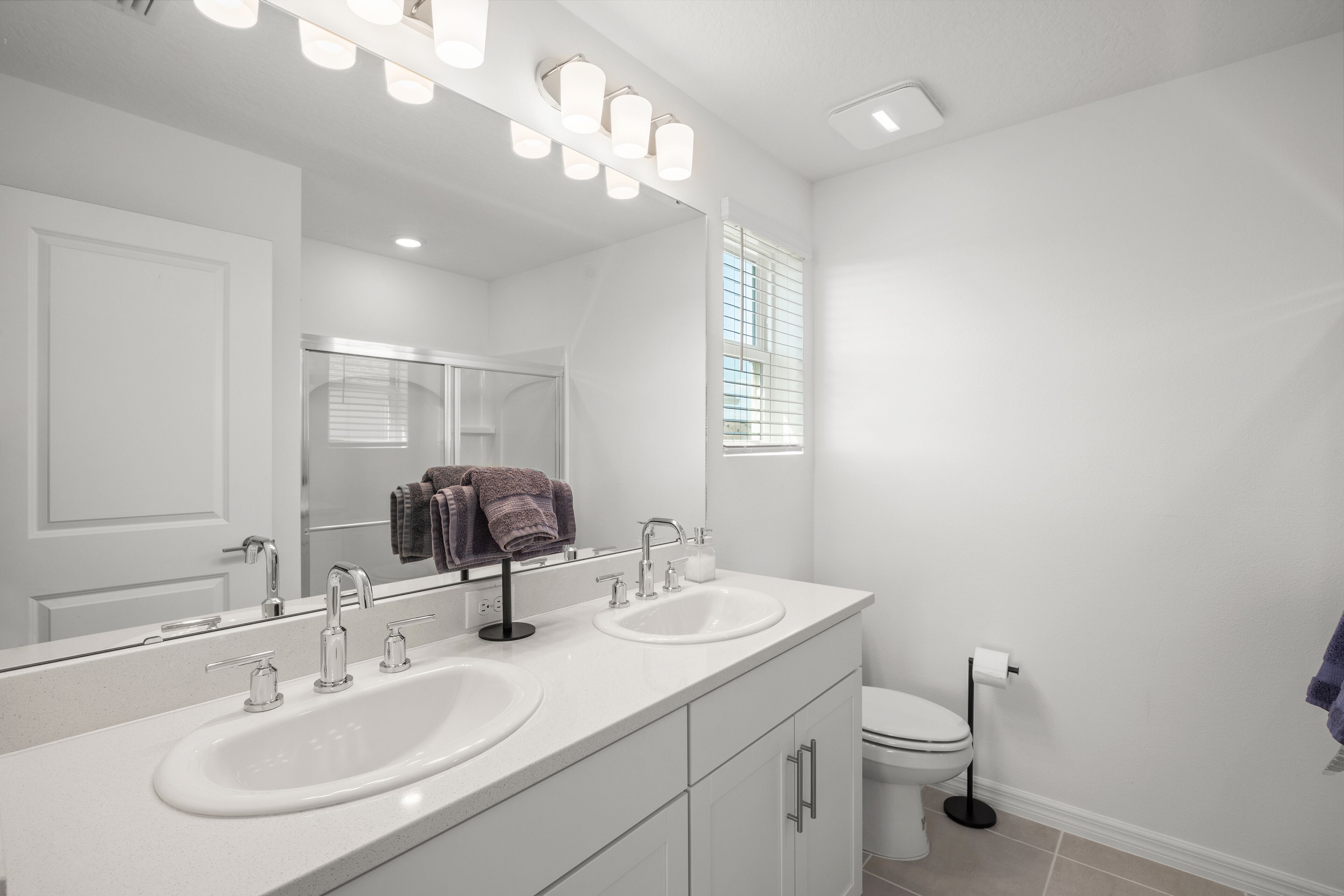 A modern bathroom with two sinks, a large mirror, and a toilet.