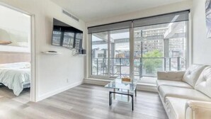 Una sala moderna con una mesa de centro de vidrio, un sofá y una cama con cubrecama blanco.