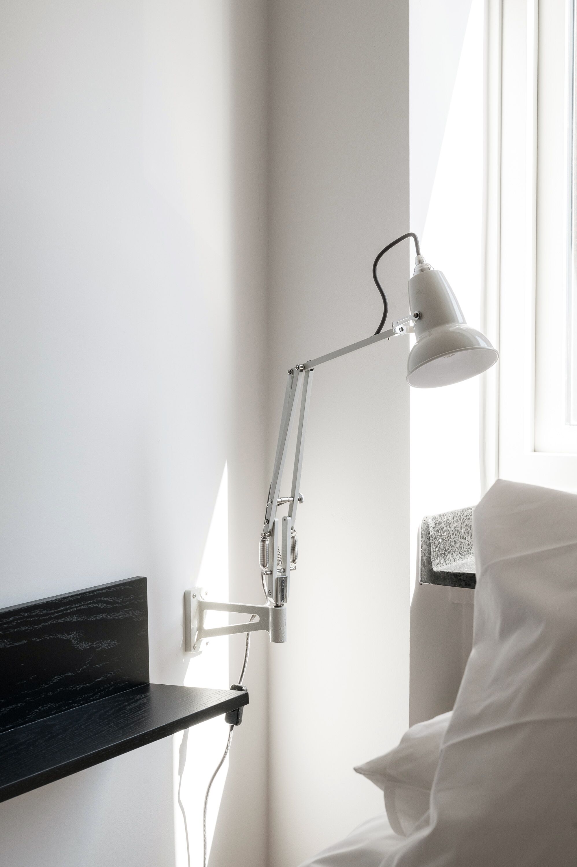 Una camera moderna con una parete bianca, uno scaffale nero, un letto bianco e una lampada da tavolo bianca.