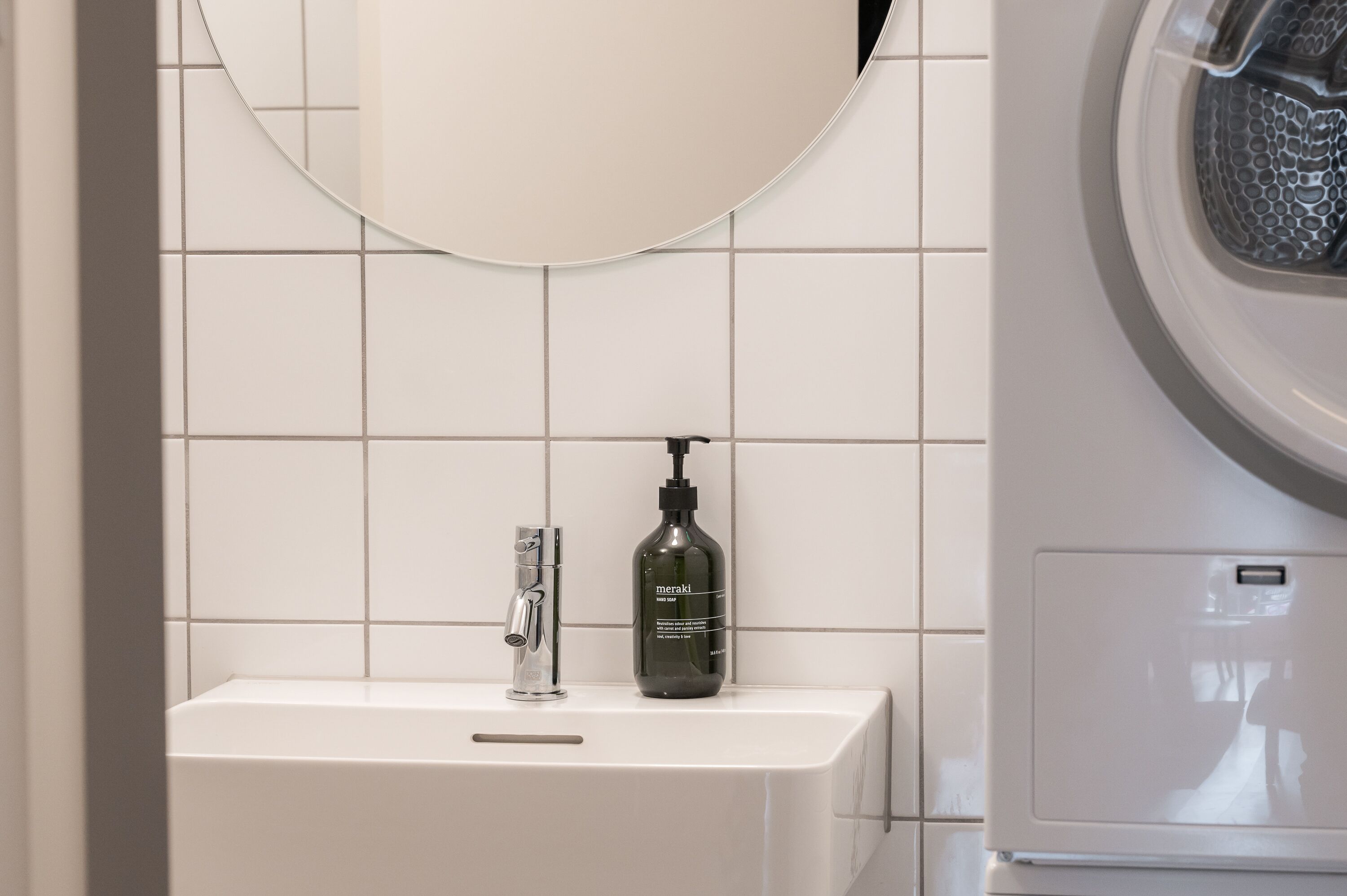 Un bagno con un lavandino bianco, uno specchio e una bottiglia di sapone Meraki.