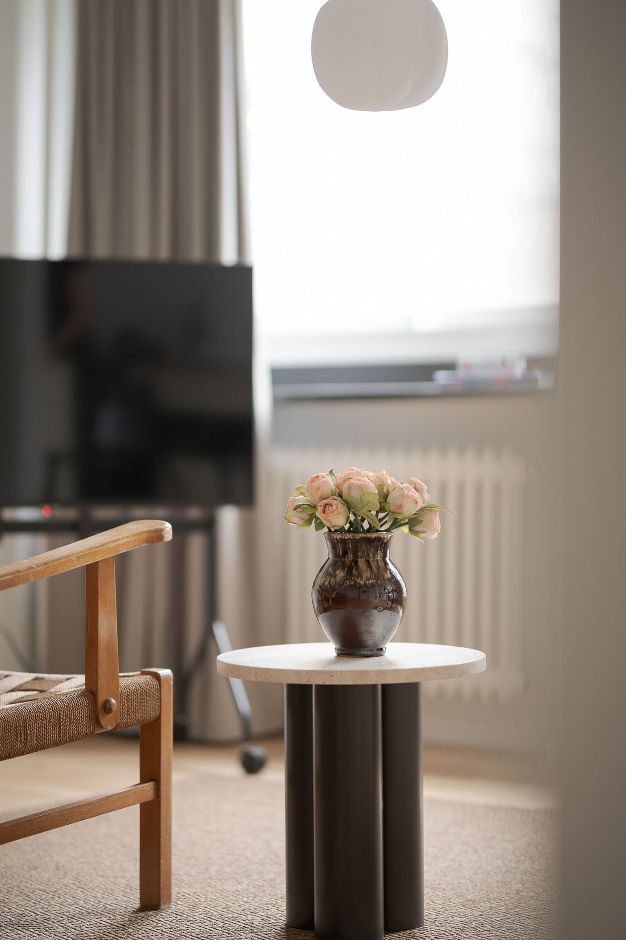 Una sala de estar moderna con una mesa redonda, una silla de madera y un jarrón con flores.