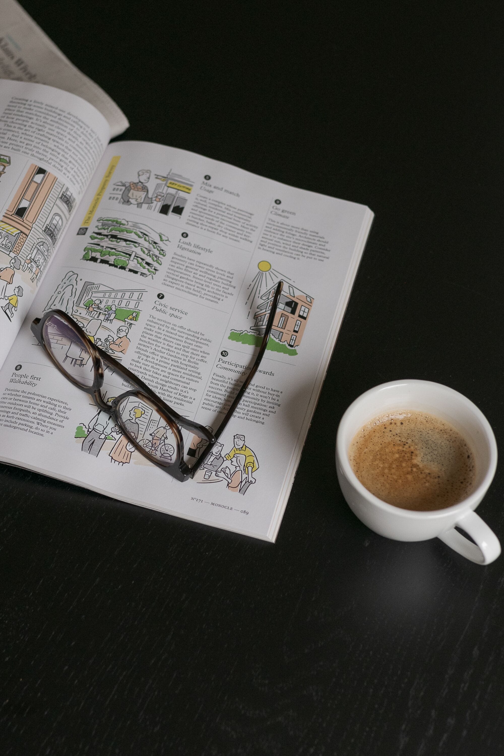 Ein offenes Buch mit Illustrationen und Text, eine Brille und eine Tasse Kaffee auf einer dunklen Oberfläche.