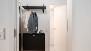 A hallway with a black cabinet, a clothing rack with a white shirt and a grey jacket, and a white door leading to a bathroom. - Queens Courtyard (Copenhagen)