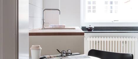 A modern kitchen with a white countertop, a black chair, and a hanging pendant light.