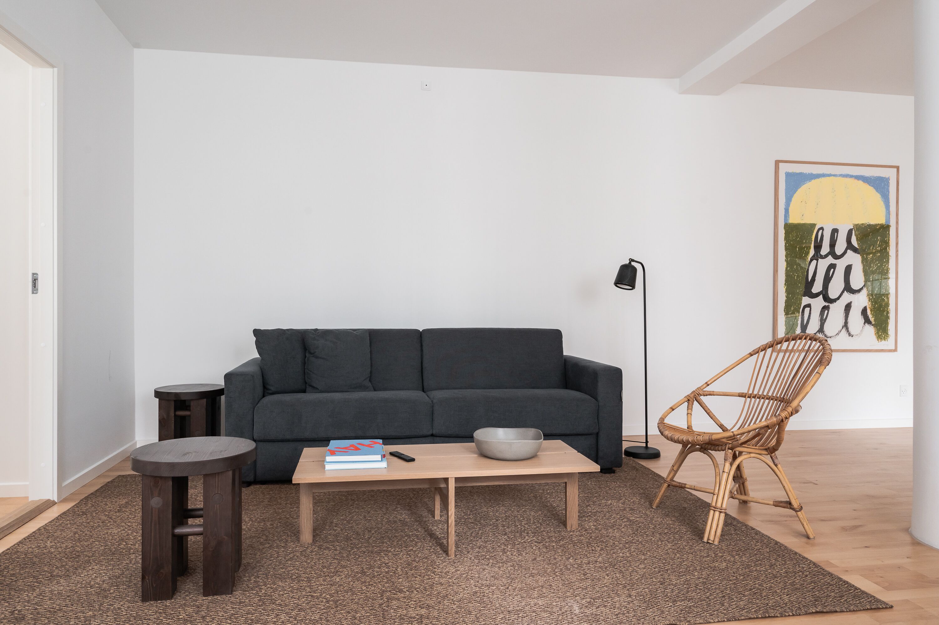 A modern living room with a dark grey sofa, a wooden coffee table, a wicker chair, and a floor lamp.