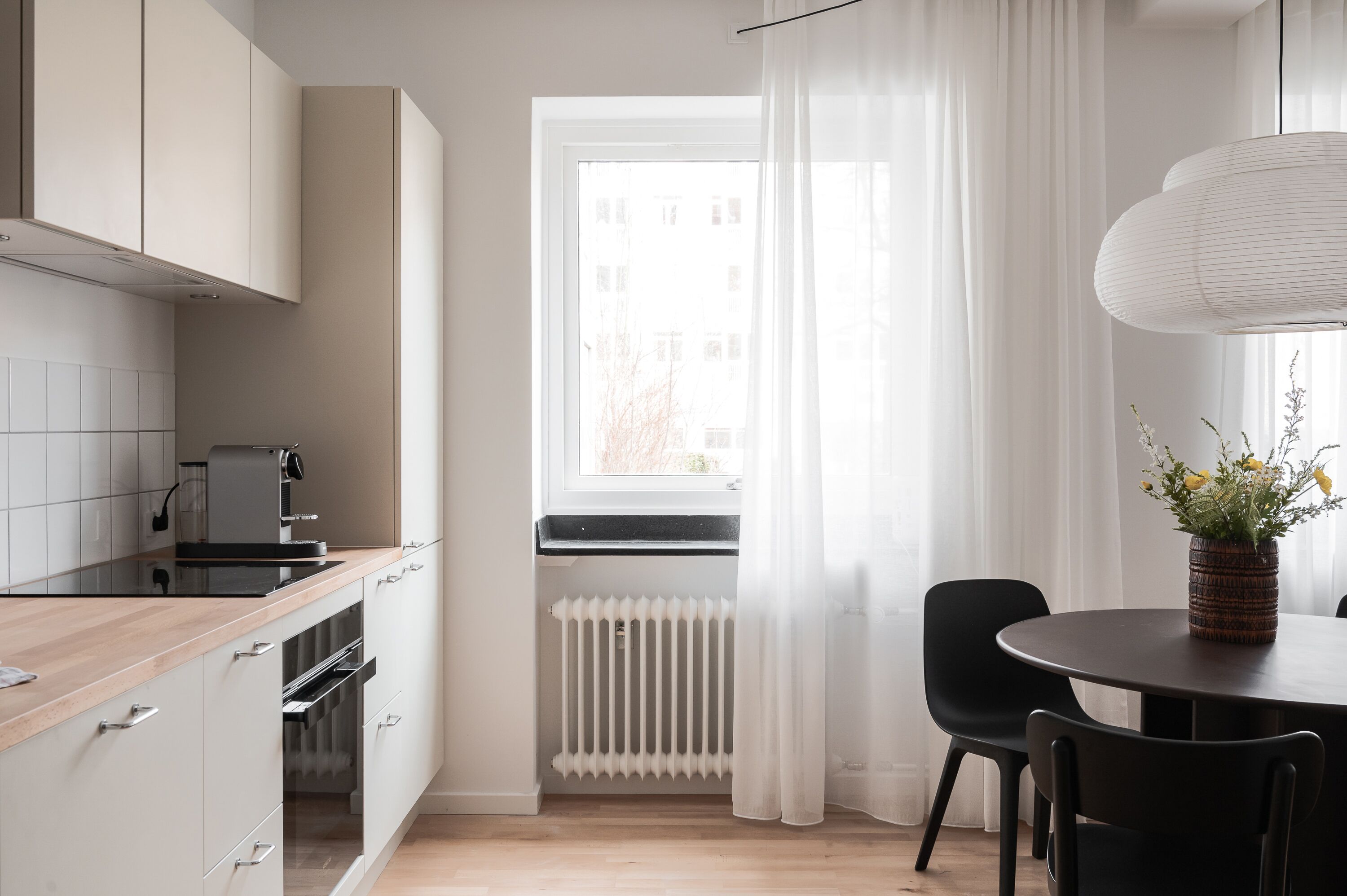 Une cuisine moderne avec des meubles blancs, un plan de travail noir et une fenêtre ornée de rideaux légers.
