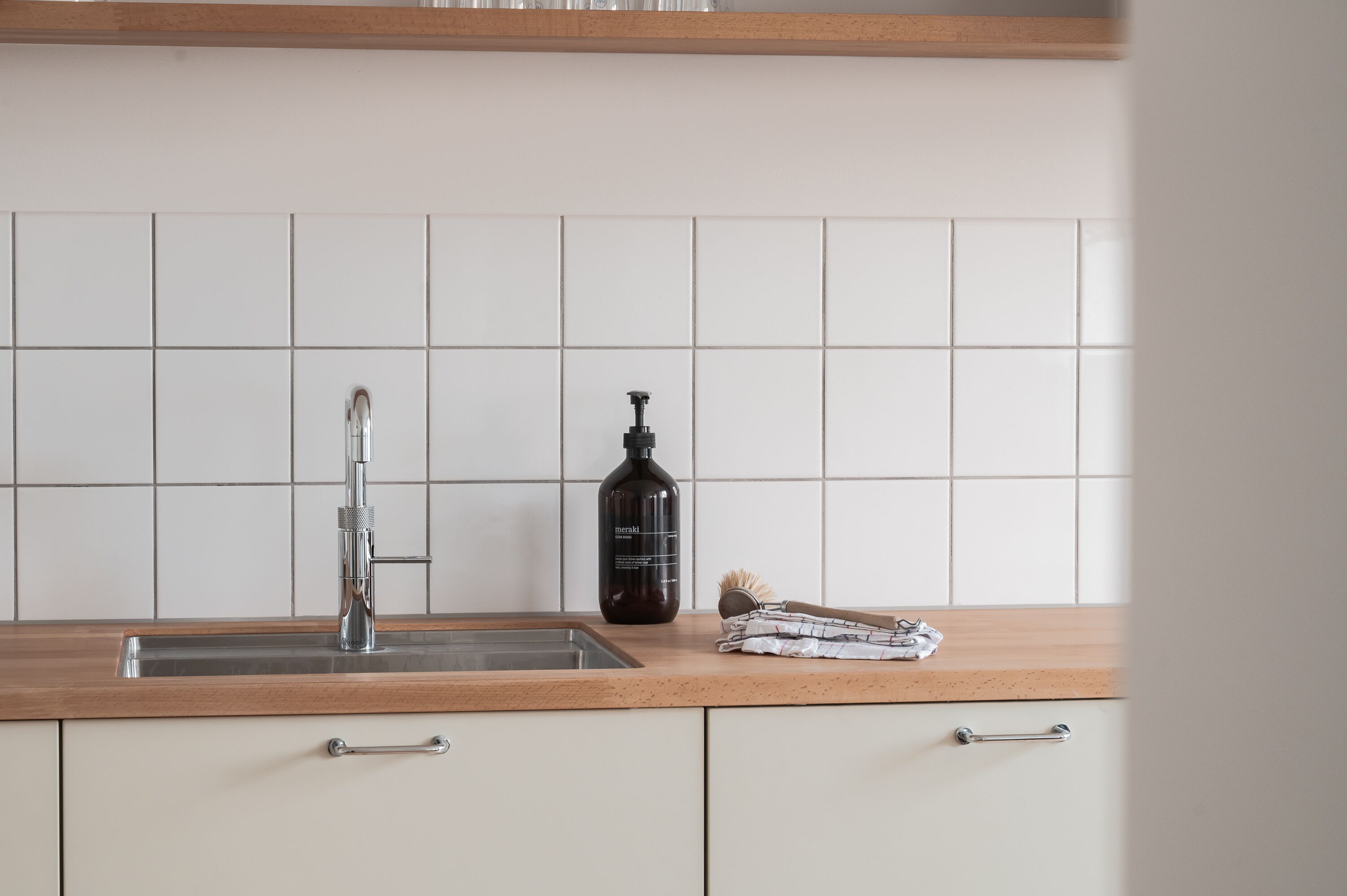 A kitchen with a stainless steel sink, a black bottle, and a wooden countertop.