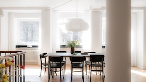 A dining area with a table and chairs, a hanging light fixture, and a view of the city through large windows. - Queens Courtyard (Copenhagen)
