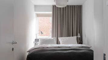 A modern hotel room with a large bed, two bedside lamps, a window with curtains, and a ceiling light fixture.