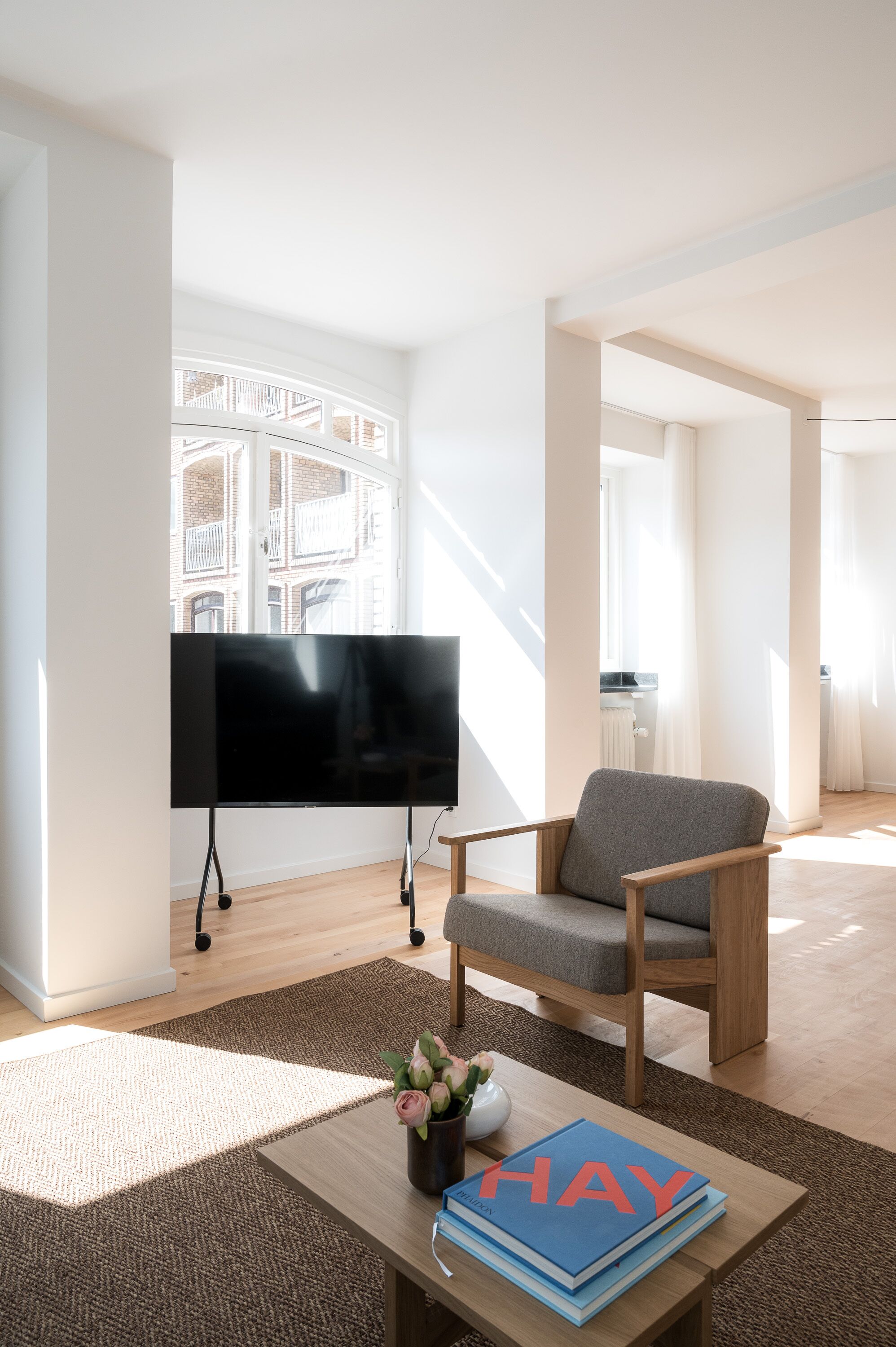 Una sala de estar moderna con un televisor de pantalla plana, un sillón gris y una mesa de centro con un libro y flores.